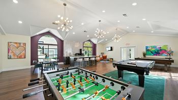A foosball table is in the middle of a room with a pool table and a ping pong table.